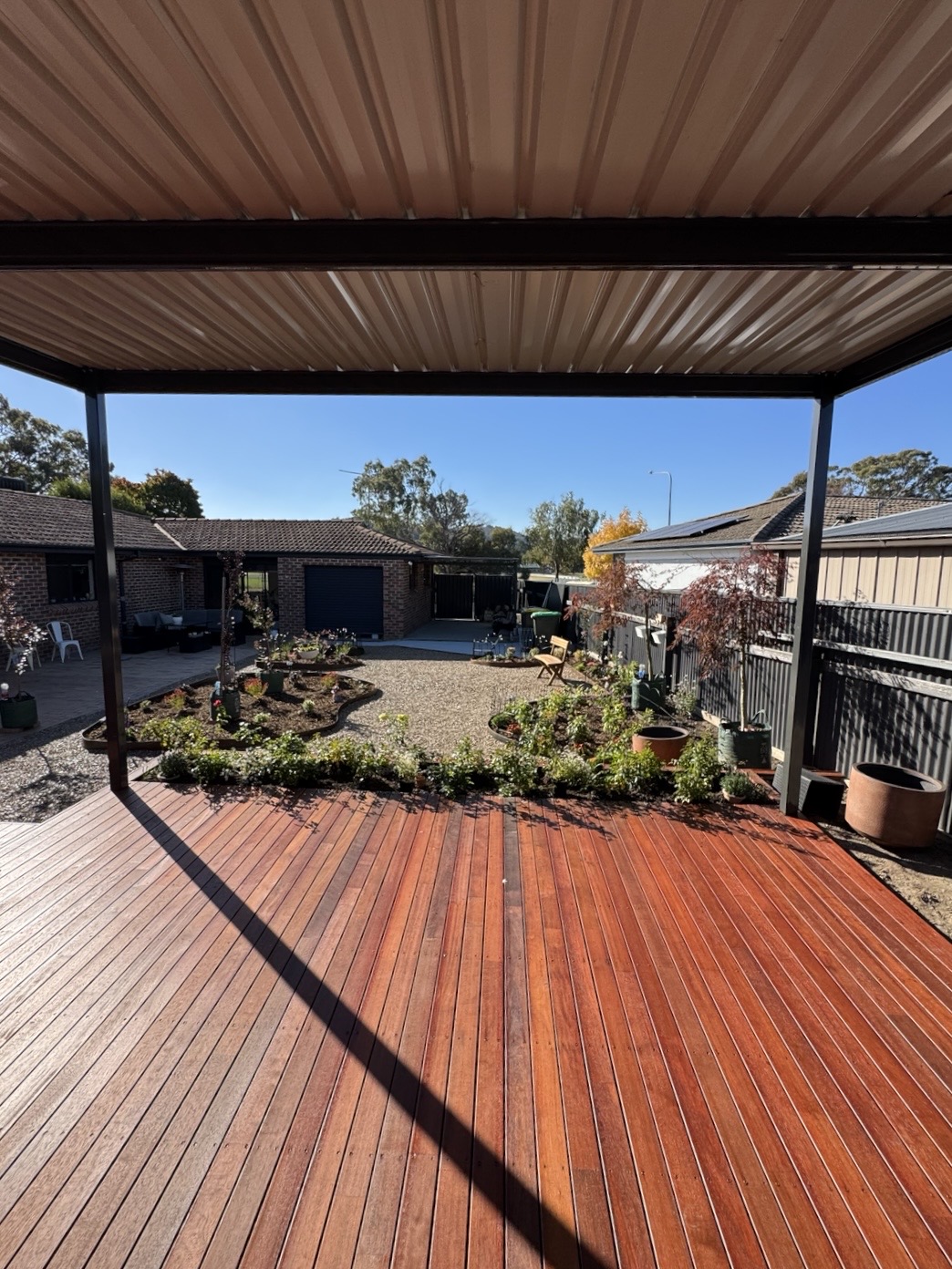 Finished hardwood deck beneath a steel-roofed pergola looking out to the garden