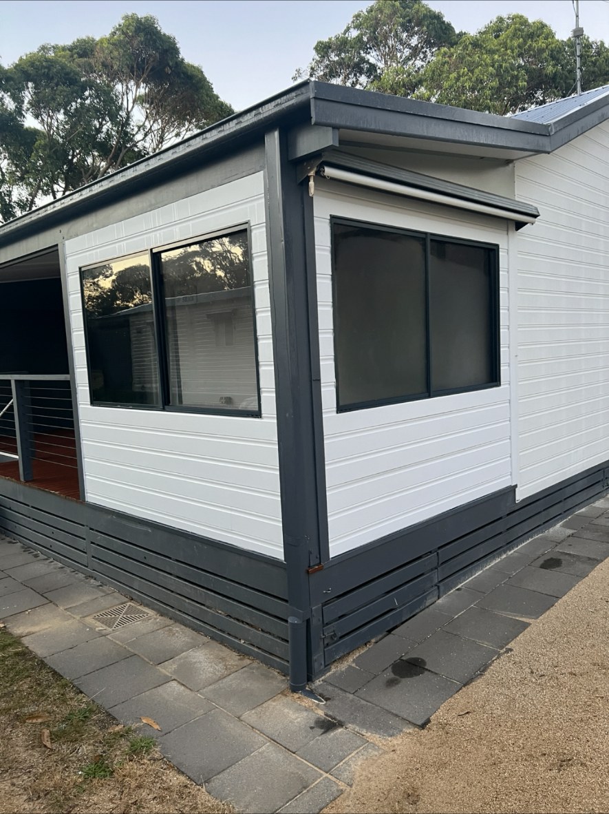 White weatherboard-profile cladding with charcoal trims on a coastal extension