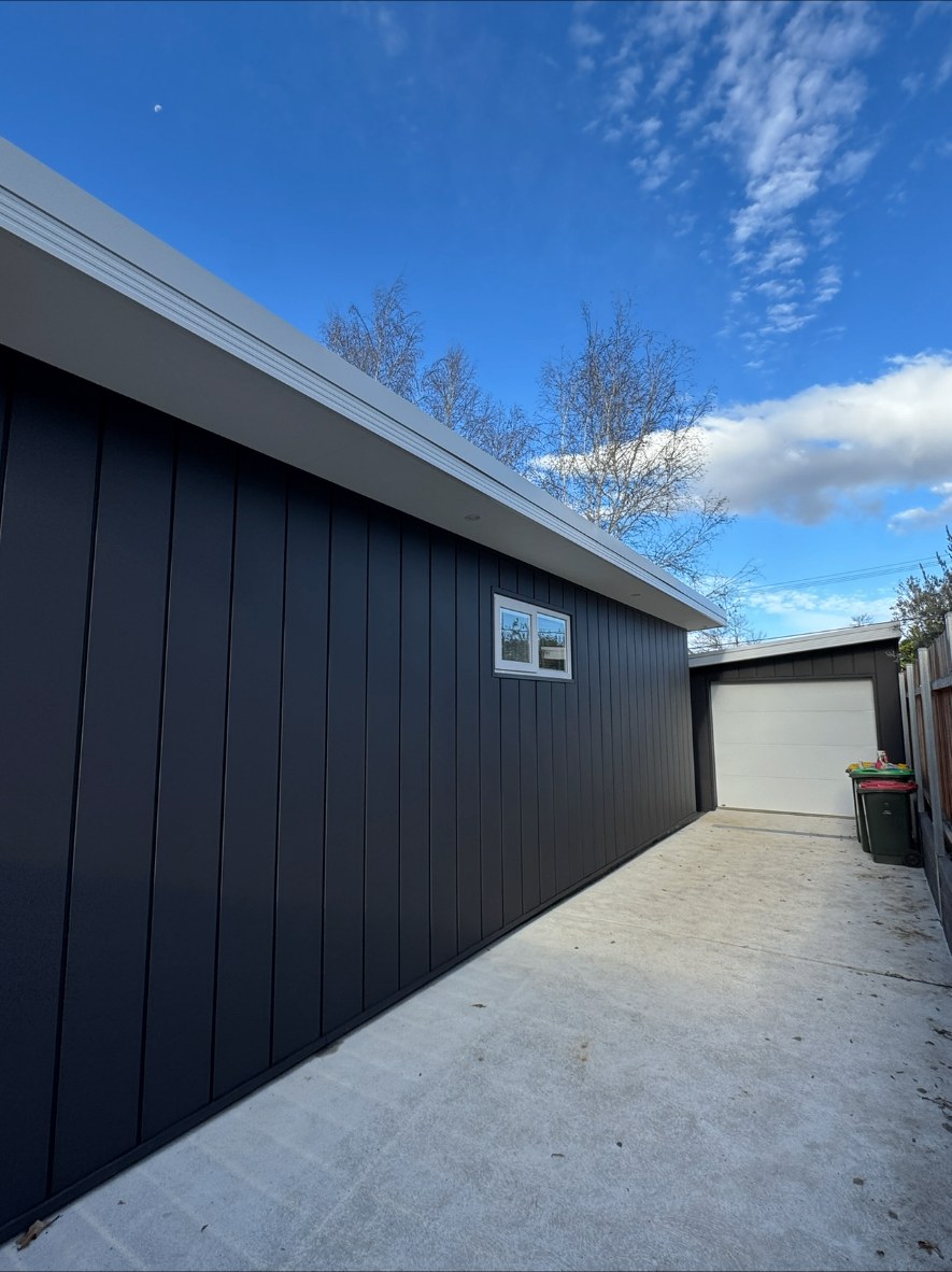 Charcoal vertical cladding along a garage wall with a new concrete driveway